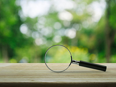 Magnifying glass on wooden table over blur tree in park
